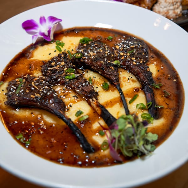 Fete's Caribbean lamb chops with polenta, garnished with sesame seeds, scallions, and a purple orchid.