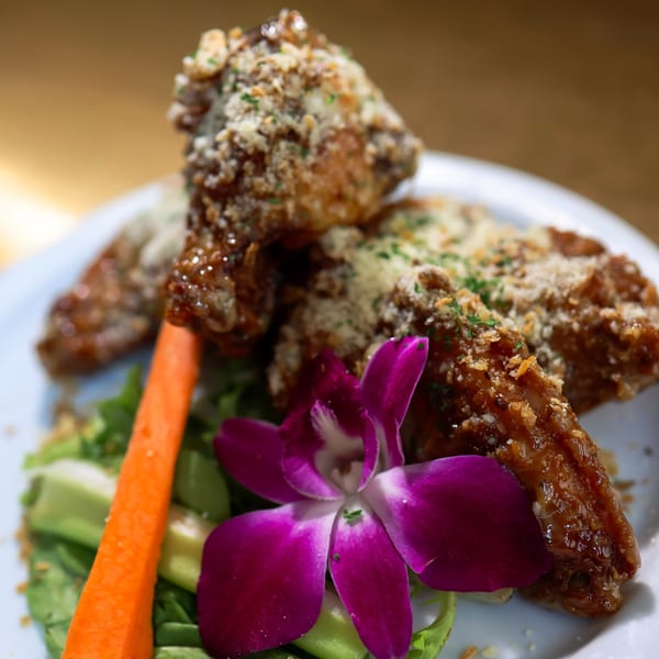 Crispy Caribbean chicken wings with a purple orchid, carrot stick, and greens on a white plate.