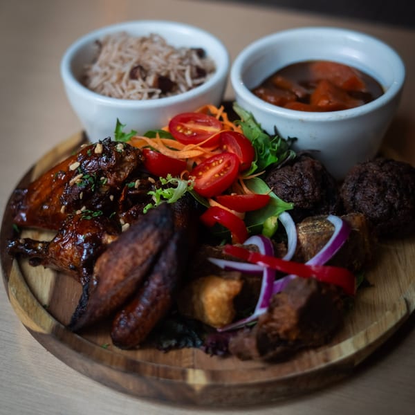 Fete's Caribbean platter with jerk chicken, rice and peas, stew, and salad on a wooden board.