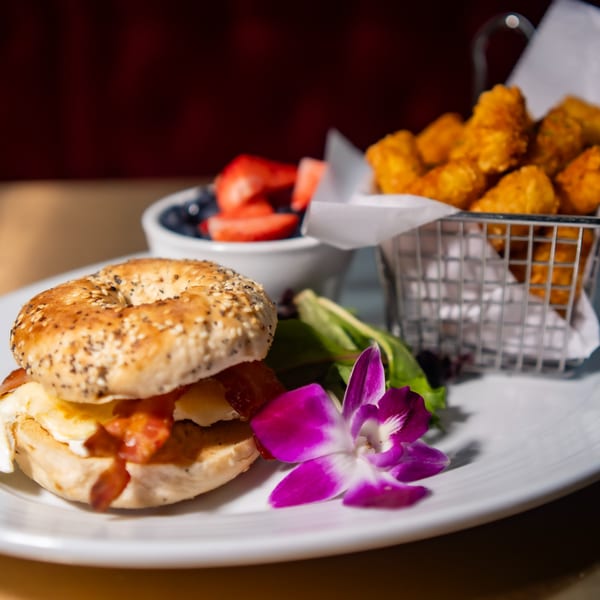 Fete's breakfast bagel sandwich with bacon, egg, and cheese, served with tots and fruit.