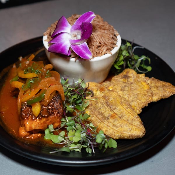 Fete's Caribbean dish with fish, peppers, rice, plantains, and microgreens, garnished with an orchid.