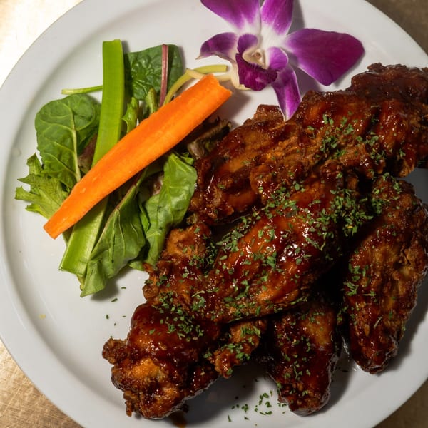 Fete's Caribbean-style chicken wings, glazed with sauce and garnished with parsley, served with a side salad and orchid.